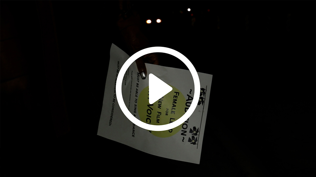 Video thumbnail of a woman holding a flyer at night.
